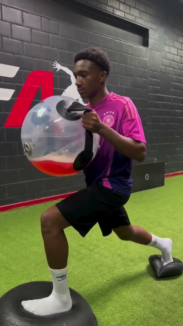 An athlete lunging while controlling a large clear water-filled ball.