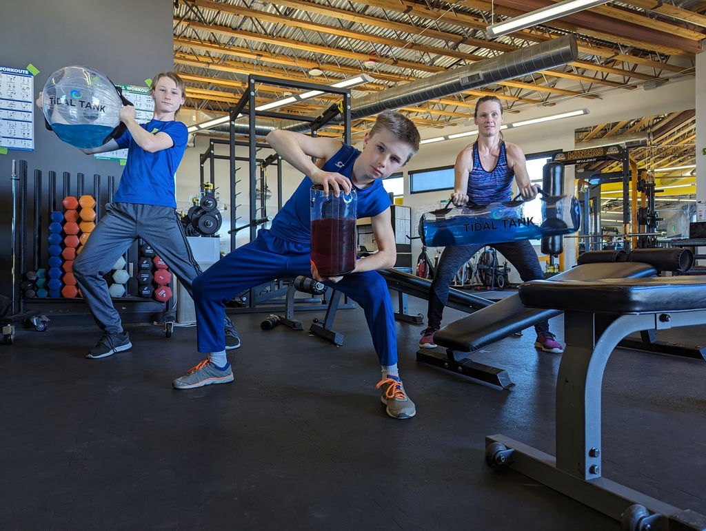 Three people training together with water-filled tubes in a gym.