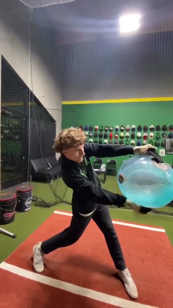 An athlete mid-rotation on a field, carrying a large water-filled sphere.