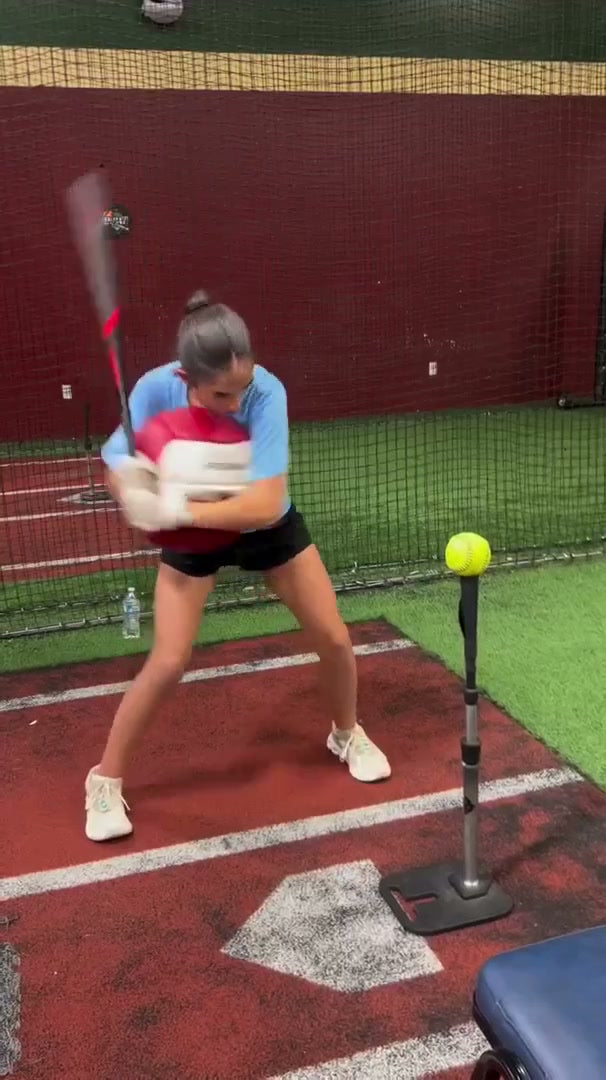 A softball hitter loading a swing against a water-filled sphere at a tee.