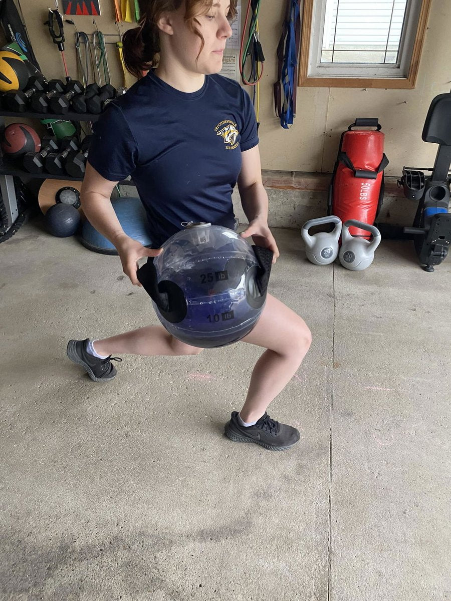 Someone driving up out of a squat with a water-filled sphere in a garage gym.