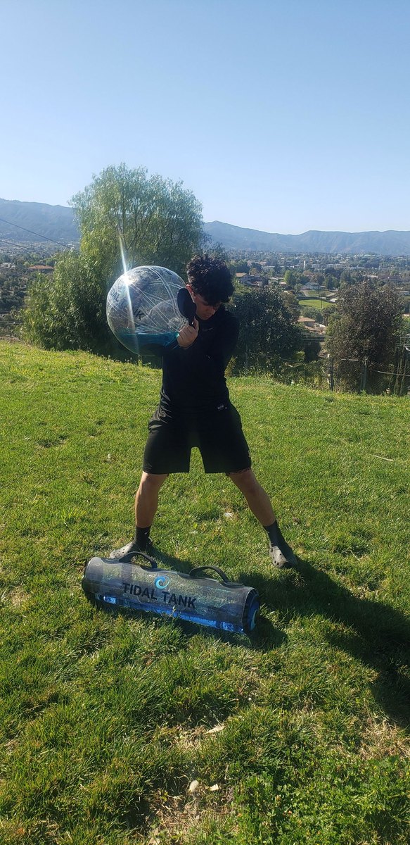 Someone holding a water-filled sphere overhead on a hilltop with a valley behind.