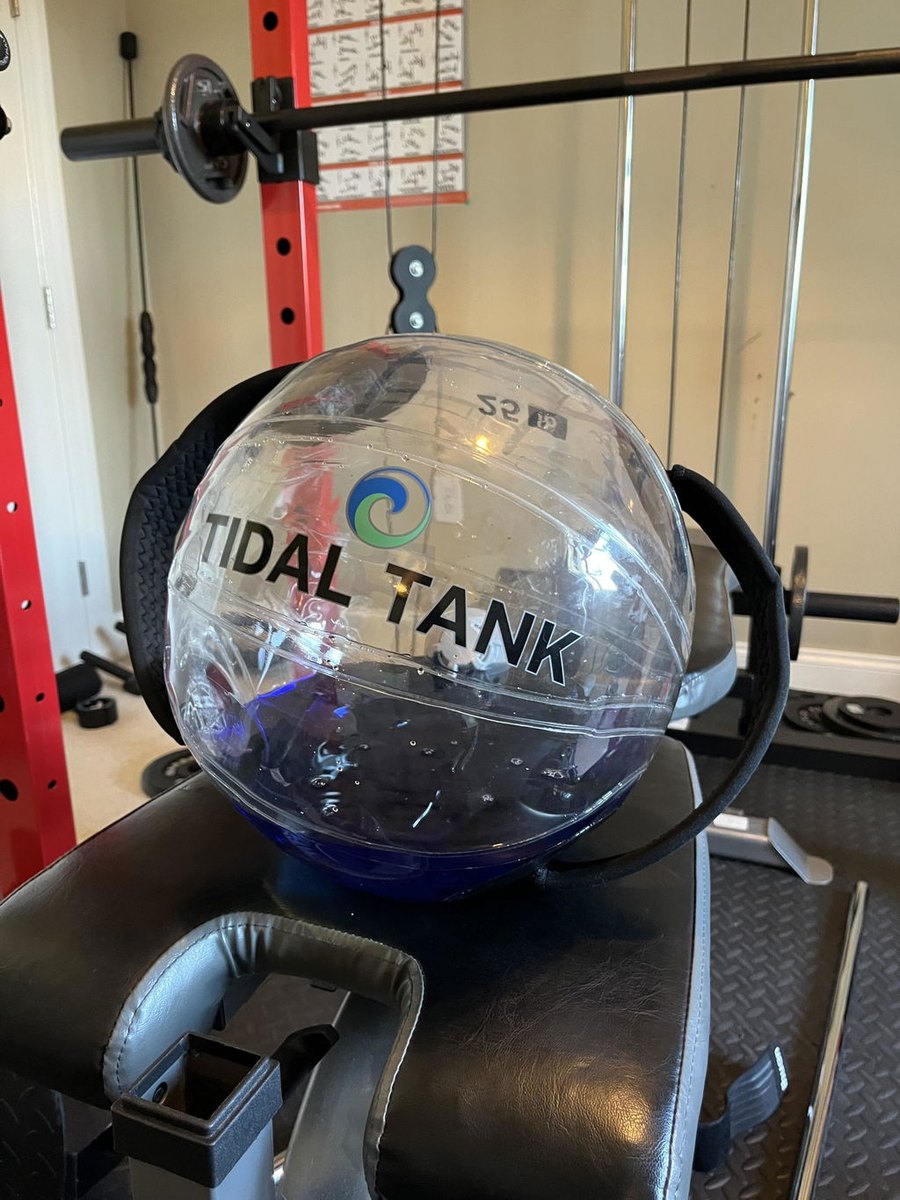 A large water-filled sphere resting on a bench in a home gym.