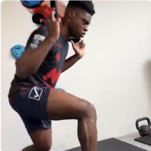 A deep lunge with a water-filled tube held overhead against a white wall.